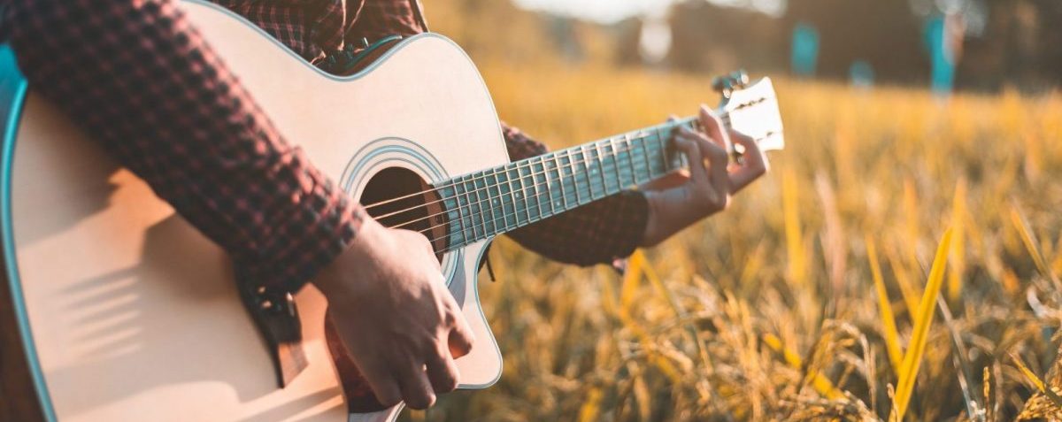 Country music, Man playing acoustic guitar in rice field, Focus on guitar strings